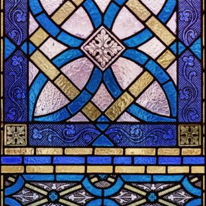 Detailed view of decorative stained glass featuring blue, gold, and white geometric shapes and floral motifs
