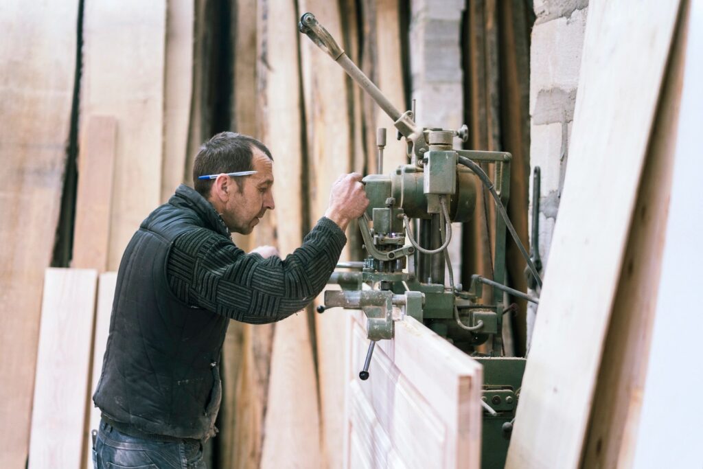 The senior 65-years-old man, sashman and carpenter, working with the industrial chain milling machine at the small wood manufacture